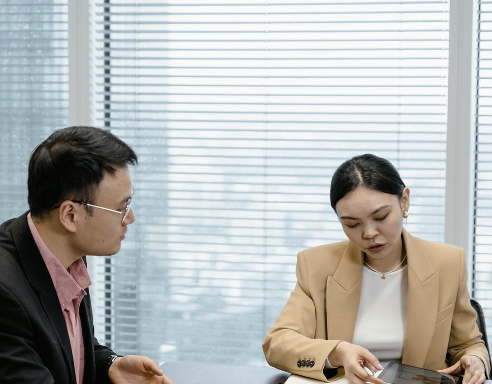 Two colleagues reviewing documents together at a window-lit table.